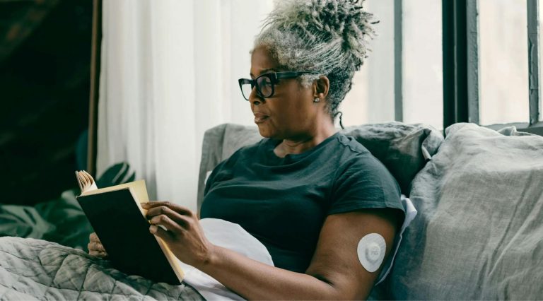 woman with diabetes wearing a cgm device on her arm reading a book