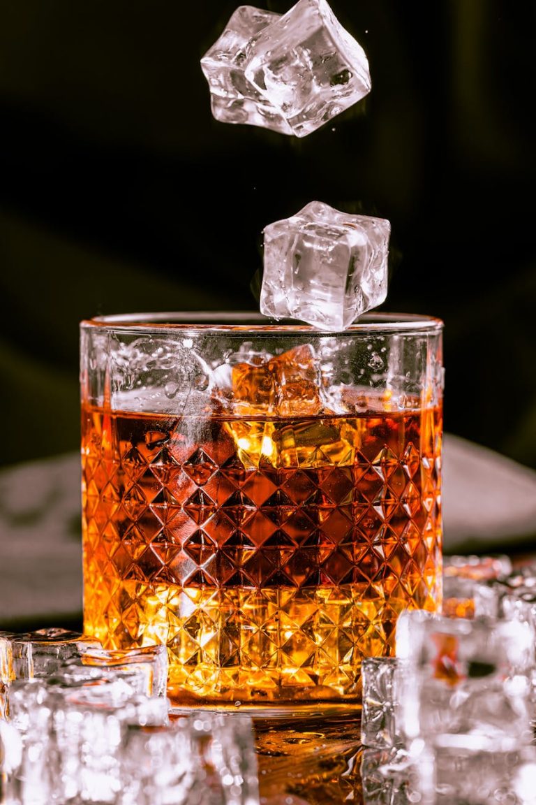 a glass of whiskey with ice cubes falling from it
