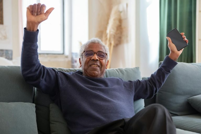 elderly man sitting on sofa while holding a cellphone